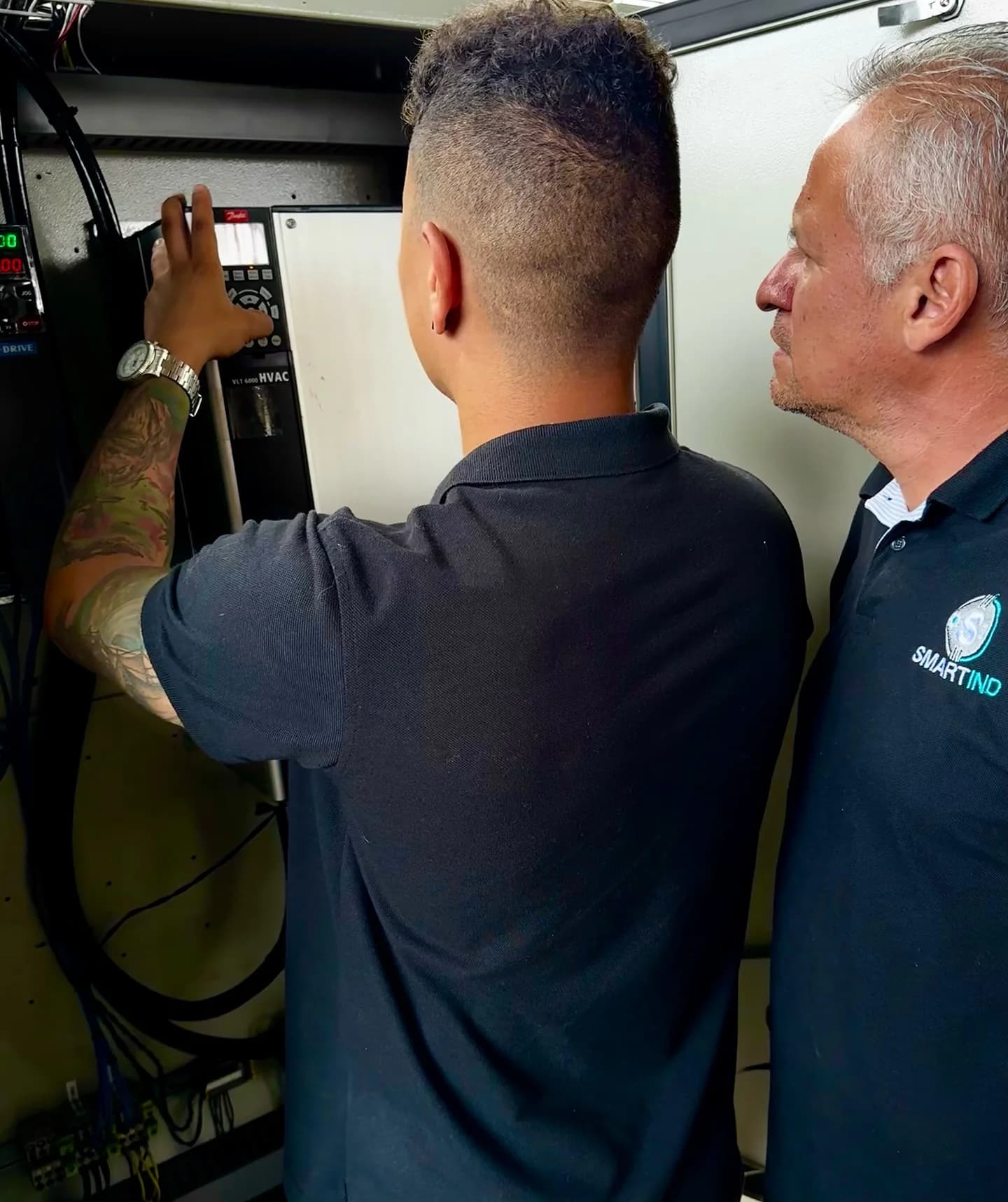 Dos técnicos de SMARTIND parametrizando un variador Danfoss VLT en el gabinete de una planta